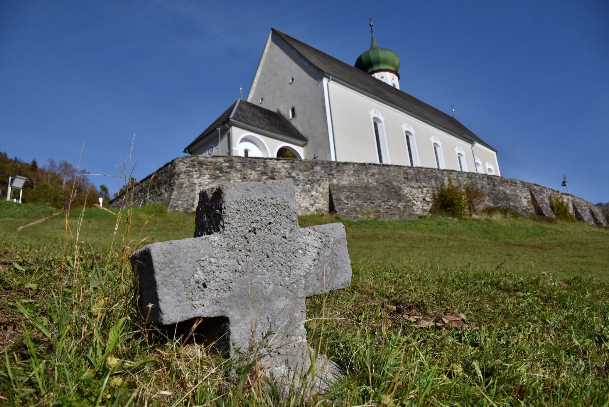 Die barocke Pfarrkirche Bartholomäberg liegt auf rund 1100 Metern Seehöhe. Das Steinkreuz befindet sich an dem schmalen Pfad, der von der Platta kommend vorbei am alten Gasthof Adler zum barocken Sakralbauwerk führt. Eine Tafel in Straßennähe informiert über das Steinkreuz; es handelt sich hierbei um ein besonderes Kulturdenkmal, so die Goethe-Universität Frankfurt.