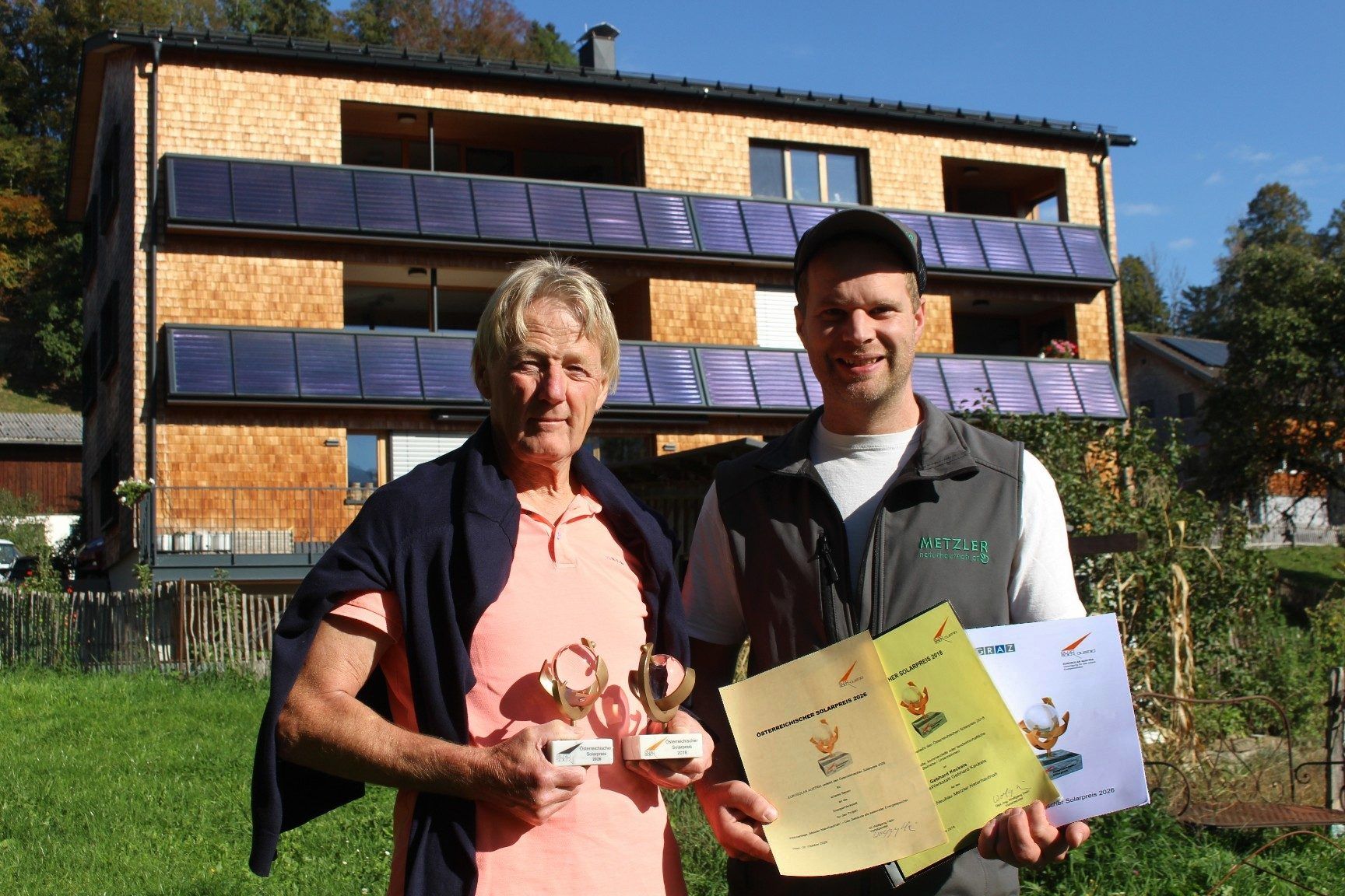 Stolz präsentieren Gebhard Keckeis (li.) und Lukas Metzler vor dem mit dem Solarpreis ausgezeichneten Wohn- und Geschäftshaus die Trophäen und Urkunden von 2026 und 2016. PETER STRAUSS