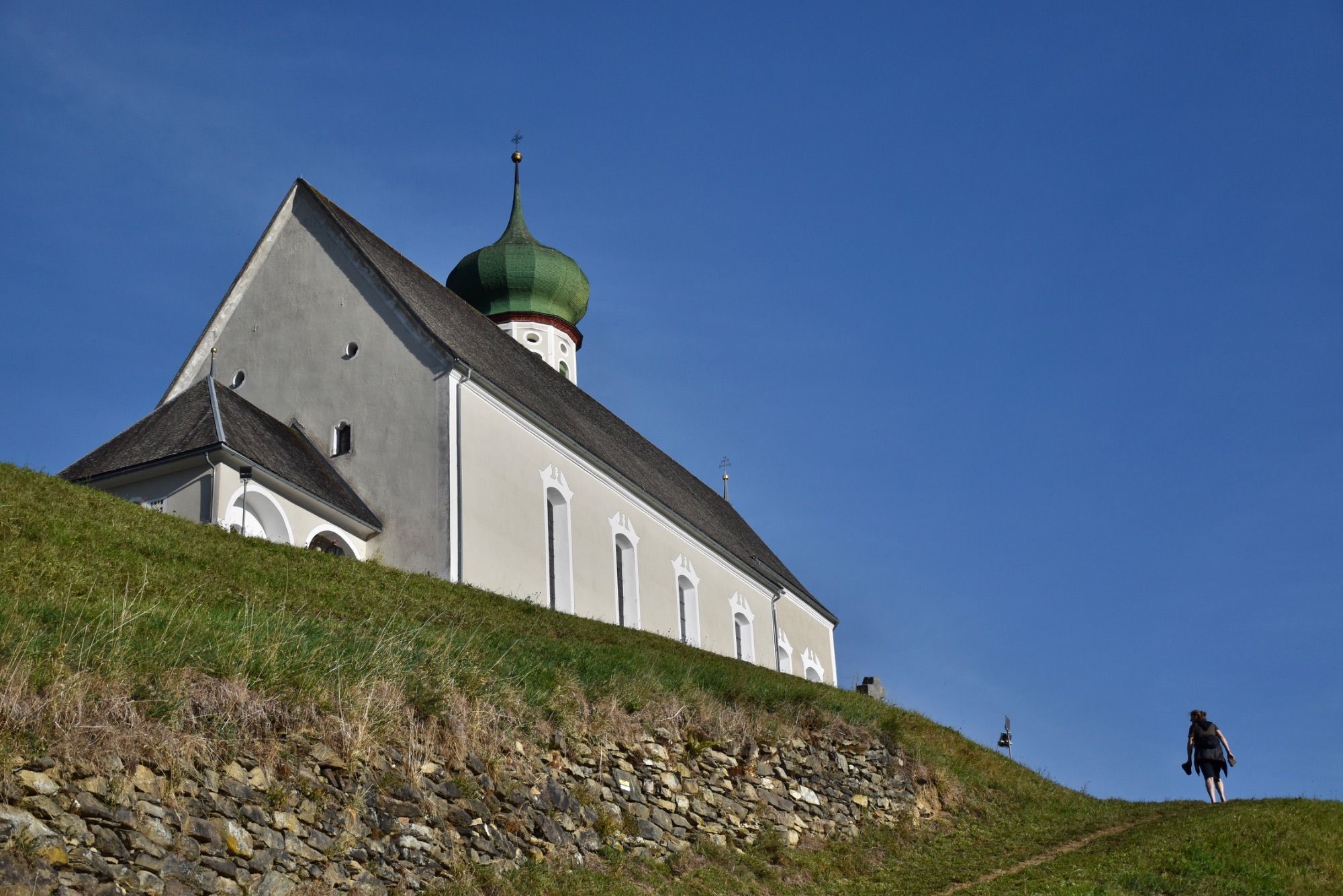 Die barocke Pfarrkirche Bartholomäberg liegt auf rund 1100 Metern Seehöhe. Das Steinkreuz befindet sich an dem schmalen Pfad, der von der Platta kommend vorbei am alten Gasthof Adler zum barocken Sakralbauwerk führt. Eine Tafel in Straßennähe informiert über das Steinkreuz; es handelt sich hierbei um ein besonderes Kulturdenkmal, so die Goethe-Universität Frankfurt.