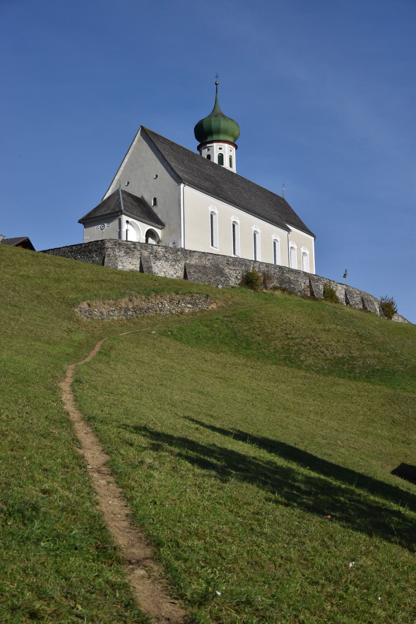 Die barocke Pfarrkirche Bartholomäberg liegt auf rund 1100 Metern Seehöhe. Das Steinkreuz befindet sich an dem schmalen Pfad, der von der Platta kommend vorbei am alten Gasthof Adler zum barocken Sakralbauwerk führt. Eine Tafel in Straßennähe informiert über das Steinkreuz; es handelt sich hierbei um ein besonderes Kulturdenkmal, so die Goethe-Universität Frankfurt.